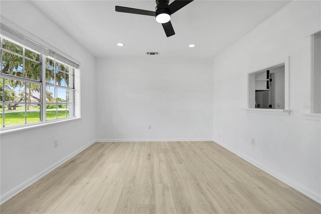 A bright, empty room features light wood-look flooring, white walls, a ceiling fan, and windows — 6625 HATCHER ROAD, LAKELAND, FL