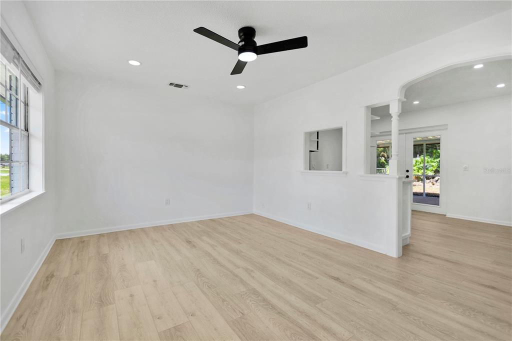 A bright, empty living room features light wood-look flooring, white walls, and a ceiling fan — 6625 HATCHER ROAD, LAKELAND, FL