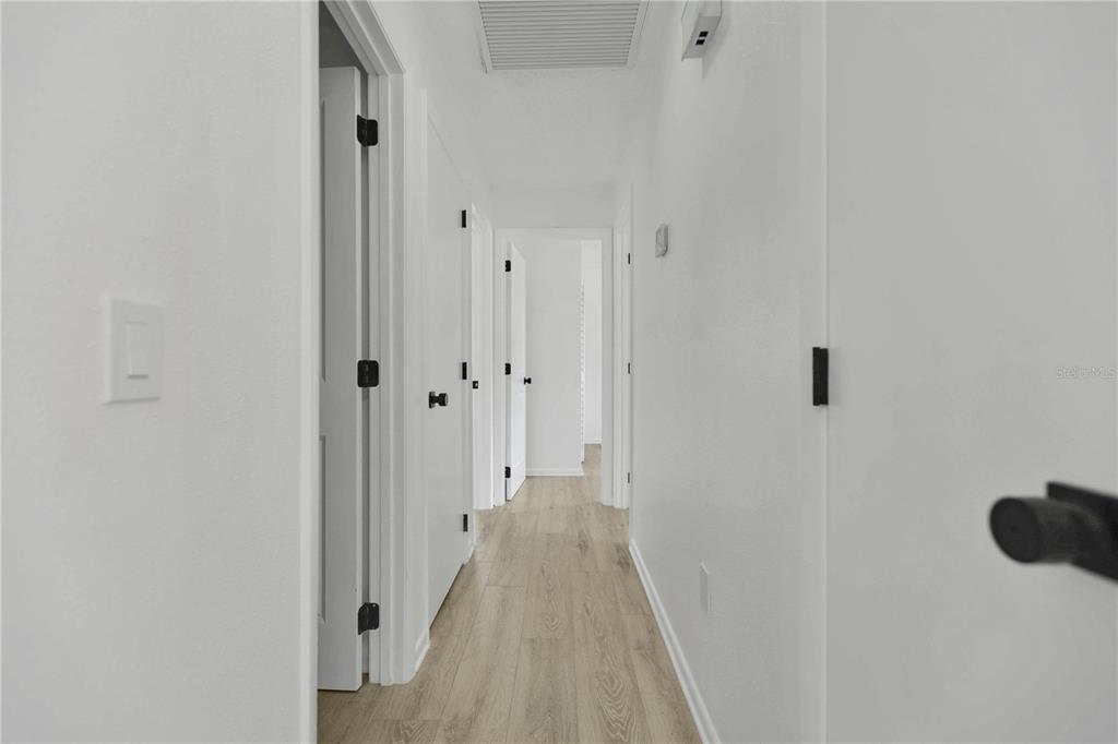 A hallway with white walls, light wood-look flooring, and several closed white doors — 6625 HATCHER ROAD, LAKELAND, FL