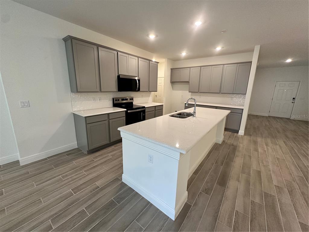 A kitchen features gray cabinets, white countertops, a central island, and wood-look tile flooring — 24 BALLARD LANE, PALM COAST, FL
