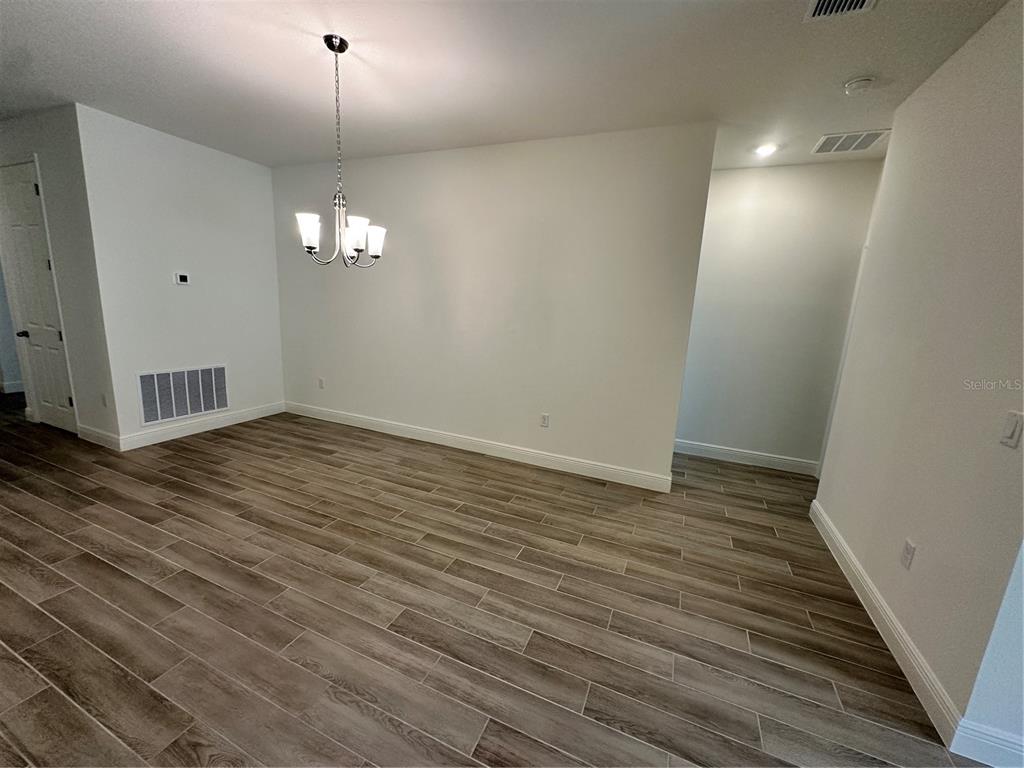 An empty dining room features a chandelier, light-colored walls, and wood-look tile flooring — 24 BALLARD LANE, PALM COAST, FL