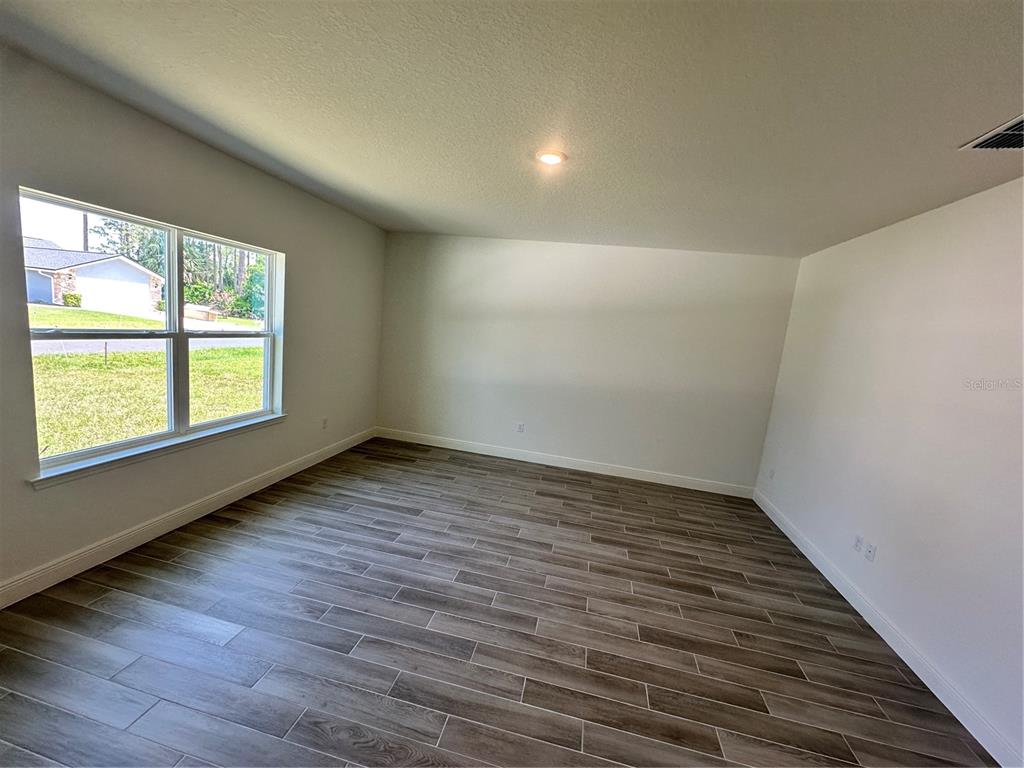 An empty room features wood-look tile flooring, white walls, and a large window — 24 BALLARD LANE, PALM COAST, FL