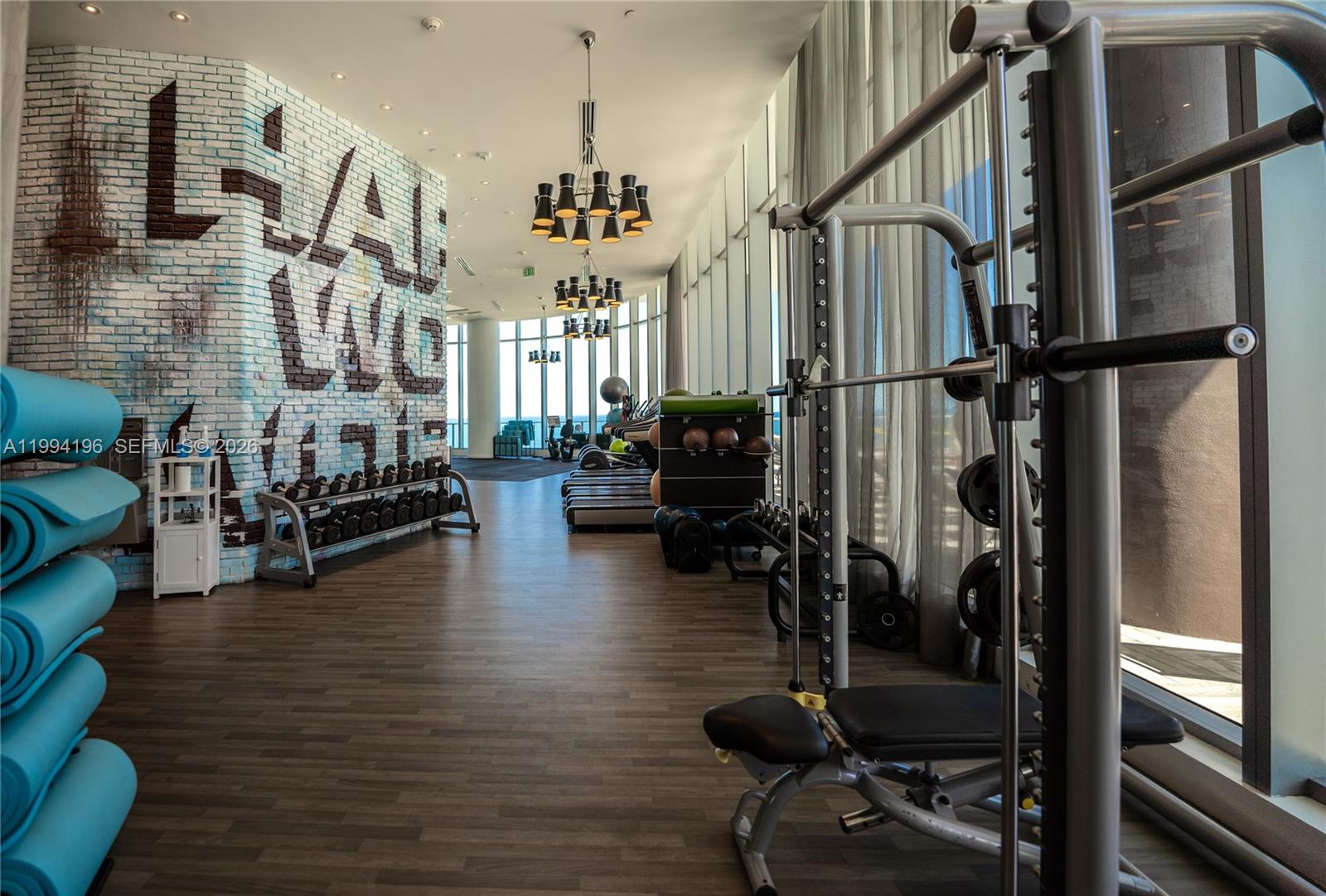 A modern gym features a brick wall with graffiti art, exercise equipment, and floor-to-ceiling windows — 4111 S Ocean Dr # 3008, Hollywood FL 33019, HOLLYWOOD, FL