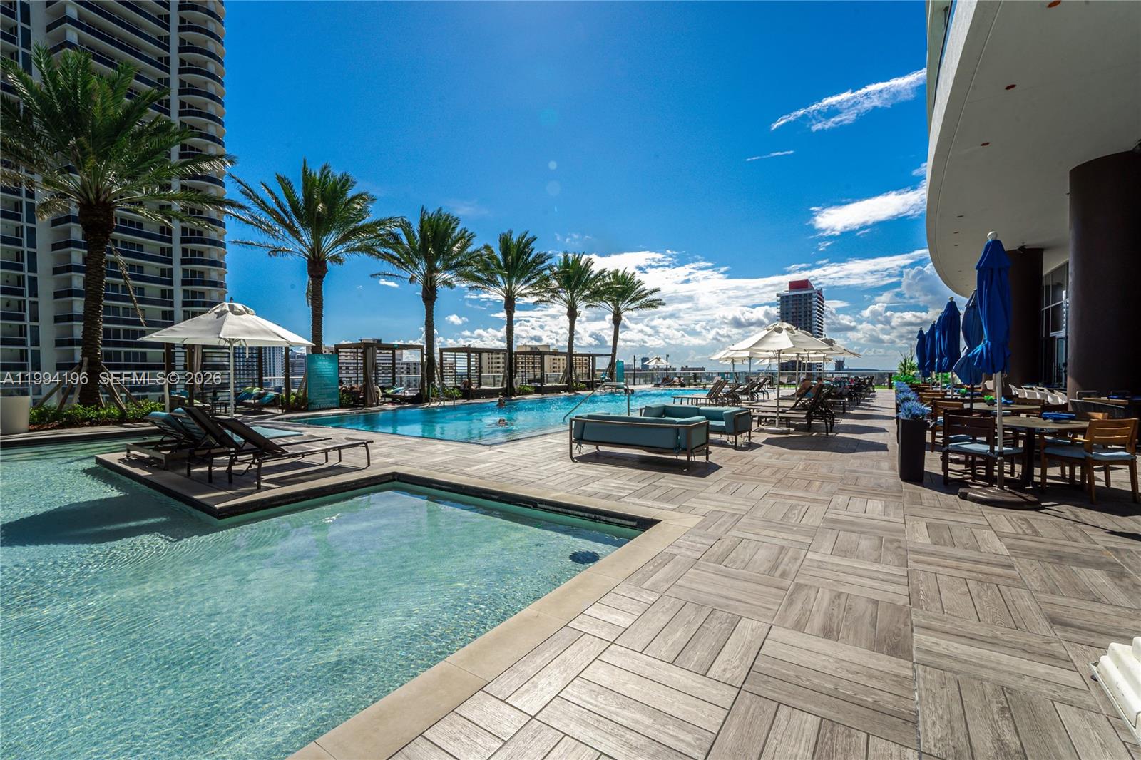 An outdoor pool deck features lounge chairs, umbrellas, and palm trees under a blue sky — 4111 S Ocean Dr # 3008, Hollywood FL 33019, HOLLYWOOD, FL