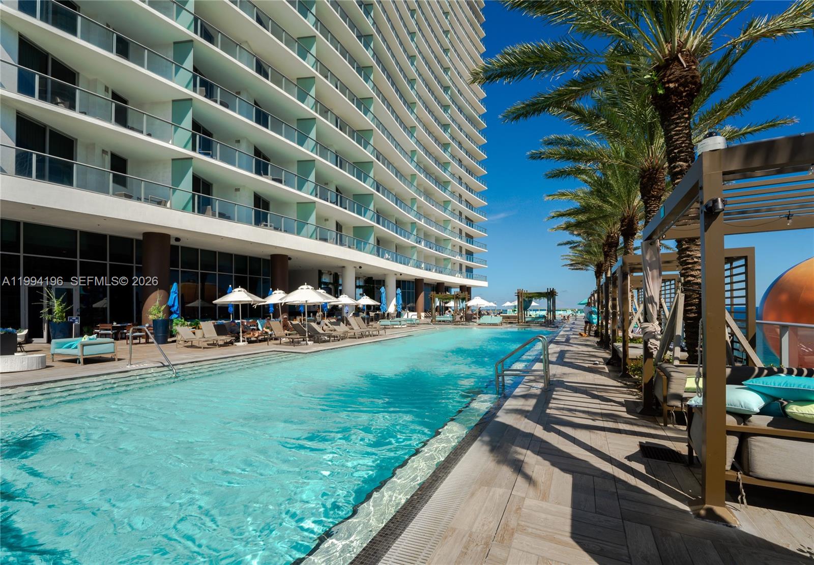 A long infinity pool runs alongside a tall modern building with multiple balconies — 4111 S Ocean Dr # 3008, Hollywood FL 33019, HOLLYWOOD, FL