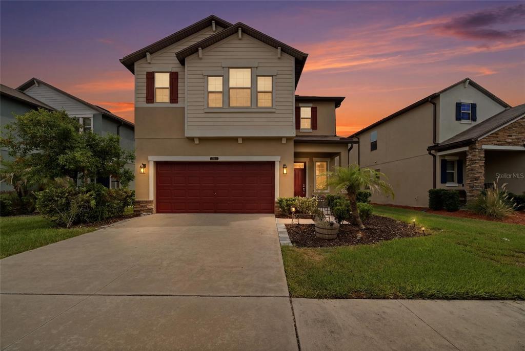A two-story suburban house with a red garage door and a concrete driveway at sunset — 8928 FLOURISH DRIVE, LAND O LAKES, FL