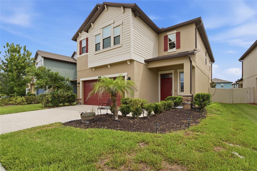 A two-story suburban house with a tan stucco exterior, red garage door, and front lawn — 8928 FLOURISH DRIVE, LAND O LAKES, FL
