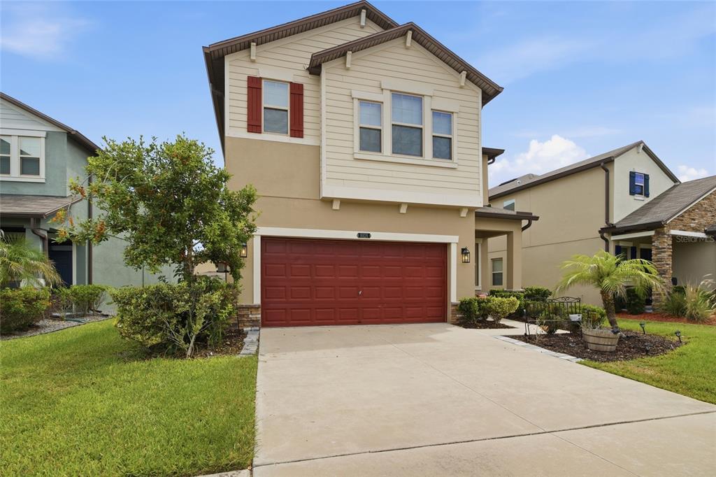 A two-story suburban house features a tan stucco exterior, a red garage door, and a driveway — 8928 FLOURISH DRIVE, LAND O LAKES, FL