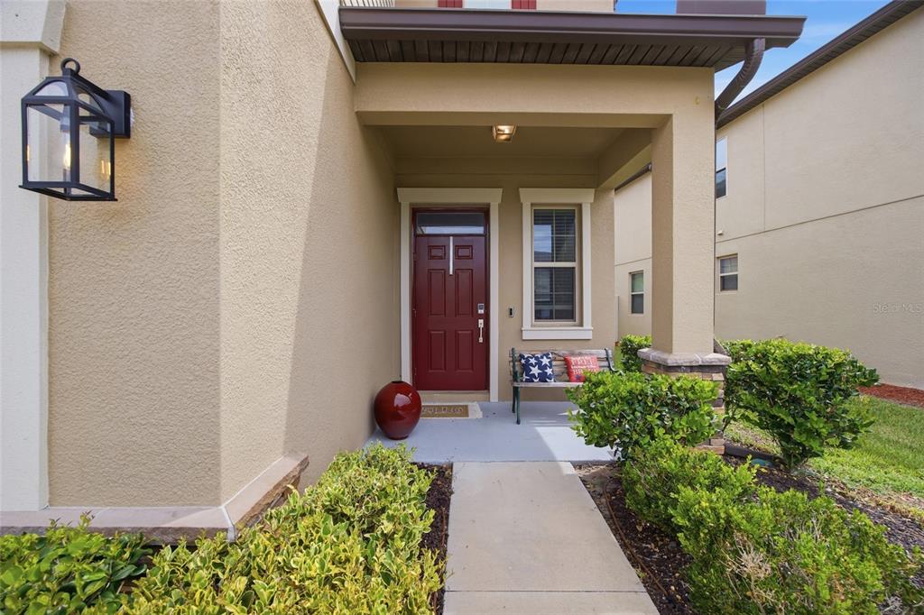 A covered entryway features a red front door, a small bench, and a concrete walkway — 8928 FLOURISH DRIVE, LAND O LAKES, FL