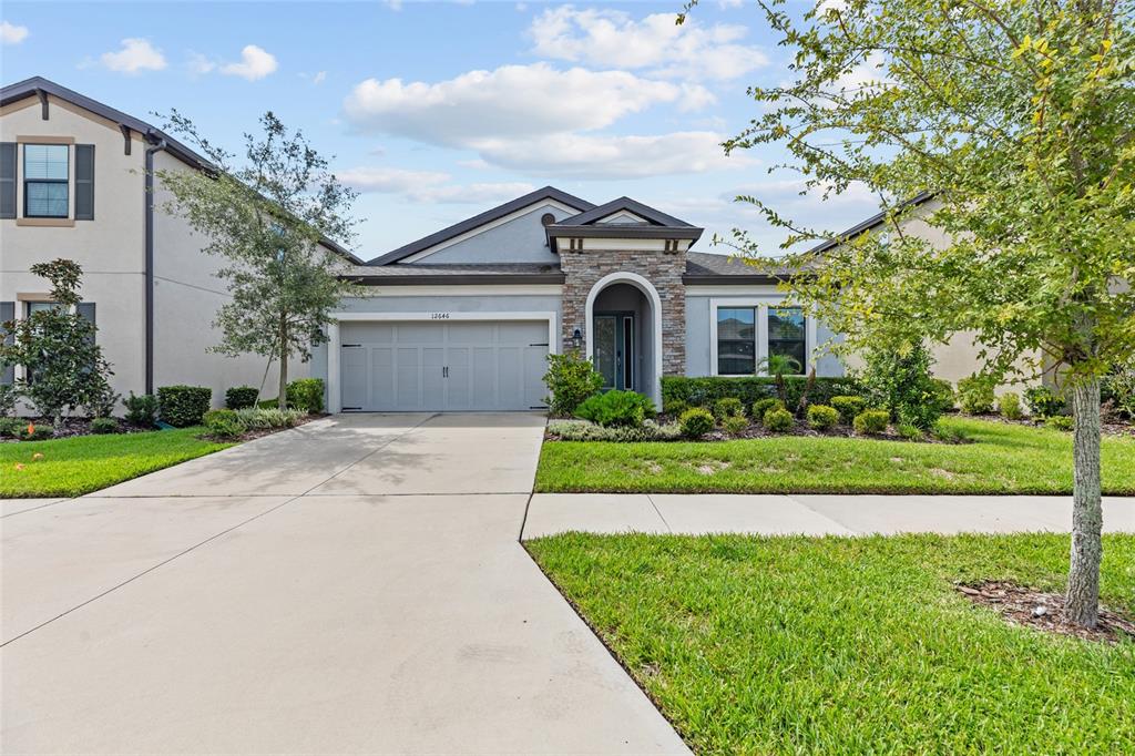 A single-story suburban house features a stone-accented entryway, a gray garage, and a manicured lawn — 12646 SHETLAND WALK DRIVE, LITHIA, FL