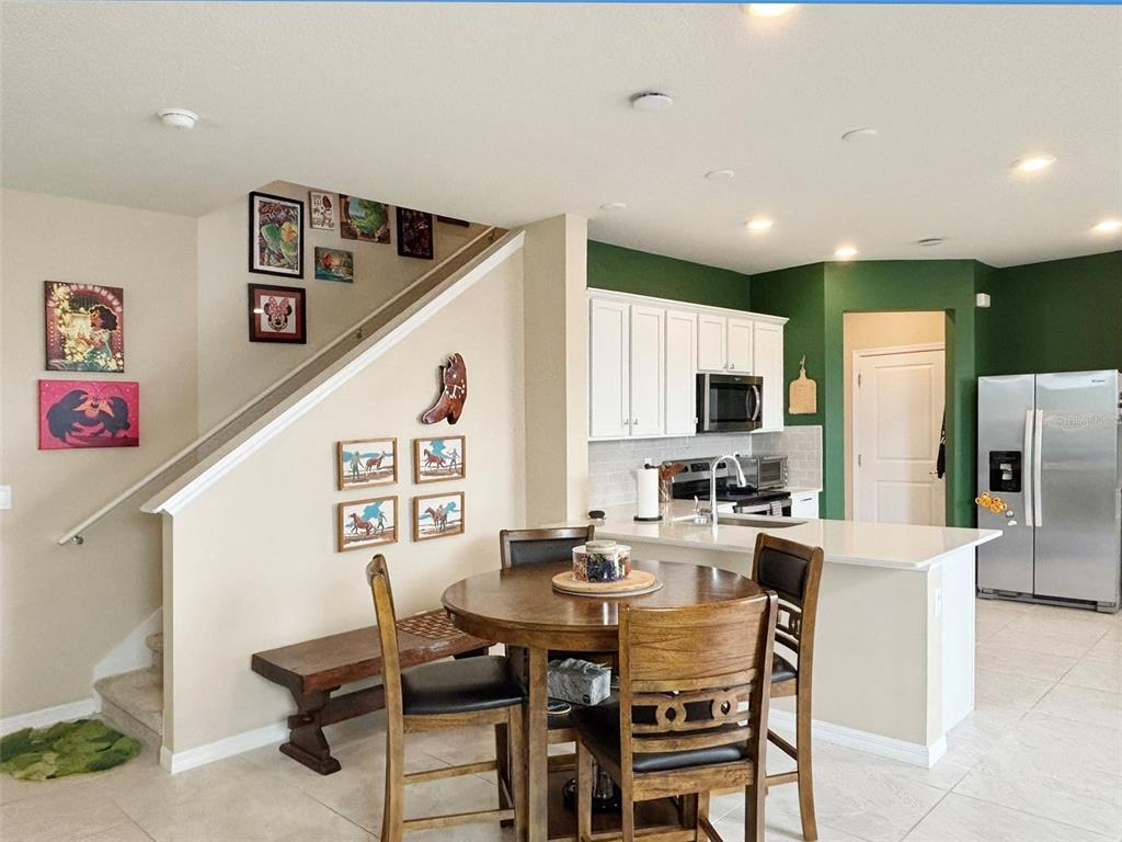 A dining area with a round wooden table sits adjacent to a kitchen with green walls — 4581 SPARKLING SHELL AVE, KISSIMMEE, FL