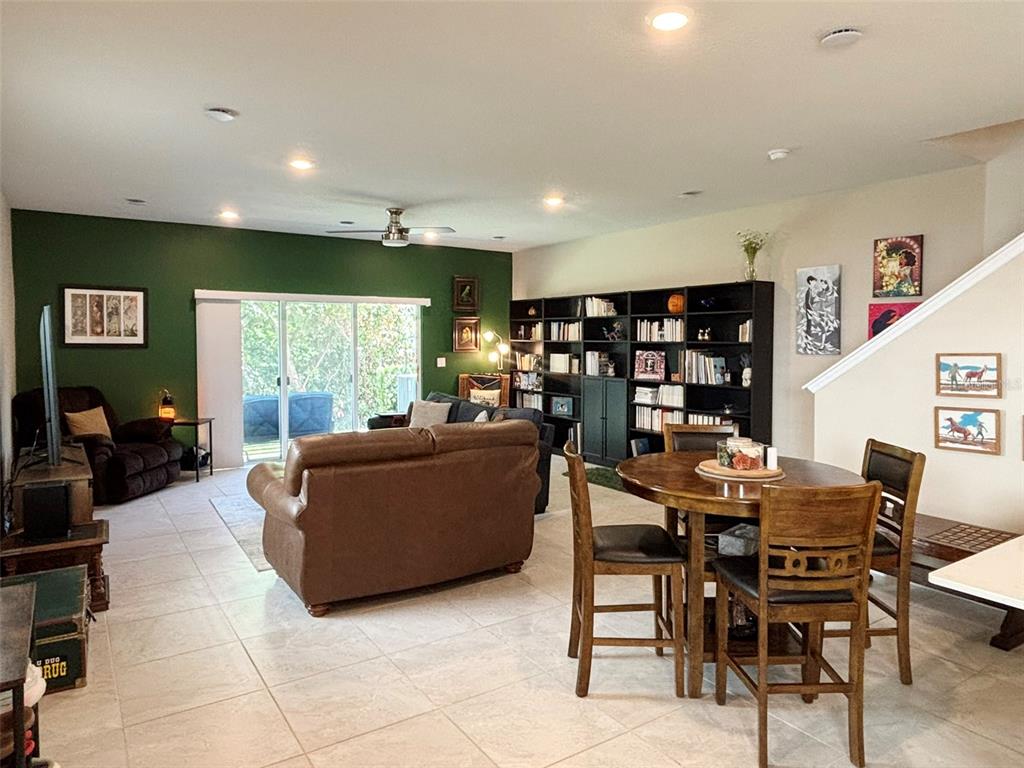 An open-concept living and dining area features a green accent wall, tile flooring, and bookshelves — 4581 SPARKLING SHELL AVE, KISSIMMEE, FL
