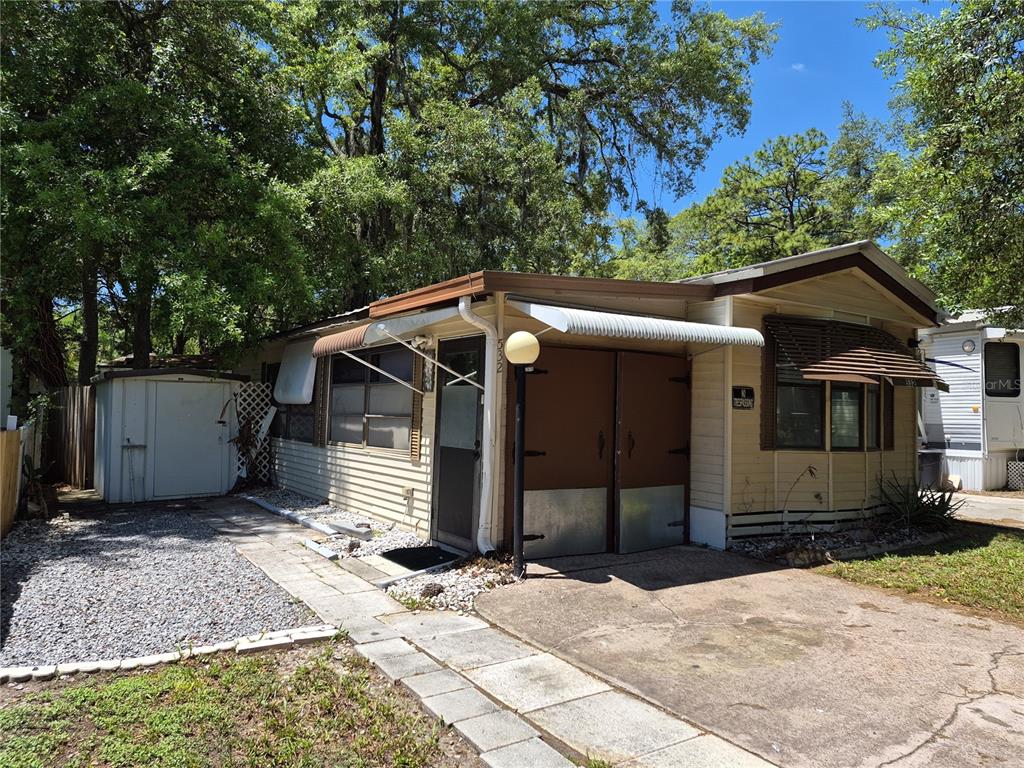 A single-story mobile home with tan siding, a concrete driveway, and a small storage shed — 3000 CLARCONA ROAD UNIT 532, APOPKA, FL