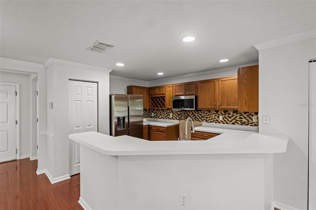 A kitchen features wood cabinets, stainless steel appliances, a mosaic backsplash, and a white breakfast bar — 2972 ROYAL TUSCAN LANE, VALRICO, FL