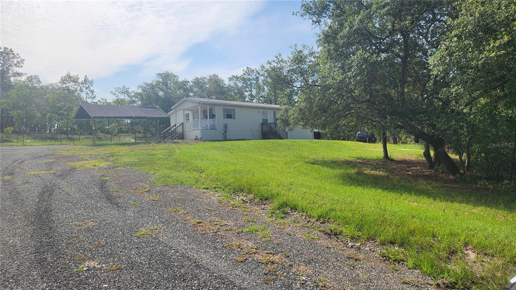 A light-colored manufactured home sits on a grassy lot with a gravel driveway and carport — 2251 SE 146TH CIRCLE, MORRISTON, FL