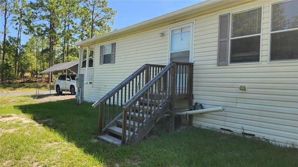 A side view of a light yellow mobile home with wooden stairs leading to a door — 2251 SE 146TH CIRCLE, MORRISTON, FL