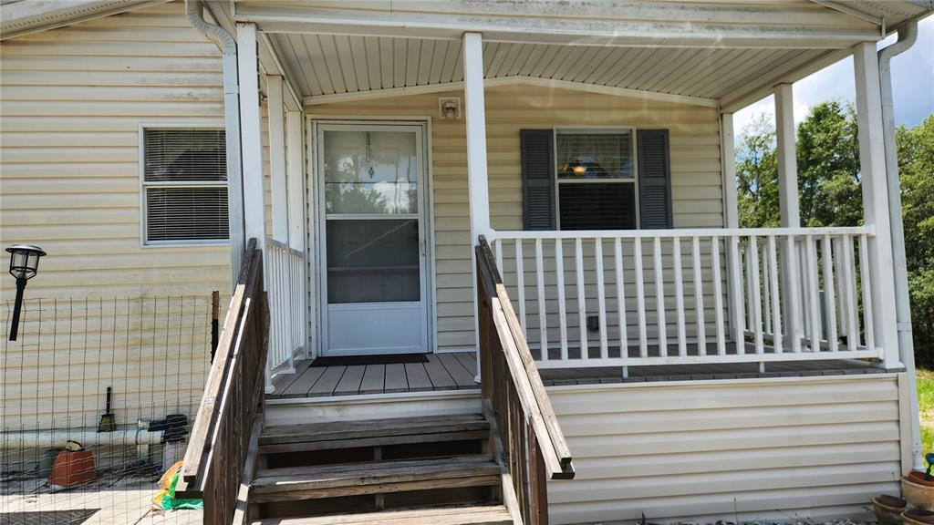A wooden staircase leads to a covered front porch with white railings and siding — 2251 SE 146TH CIRCLE, MORRISTON, FL