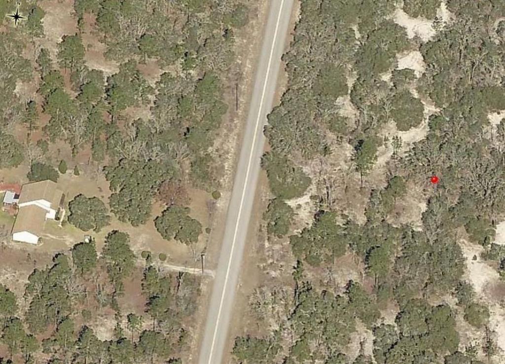 An aerial view shows a road running through a wooded area with a nearby house — Lot 27 SW HALF MOON DRIVE, DUNNELLON, FL