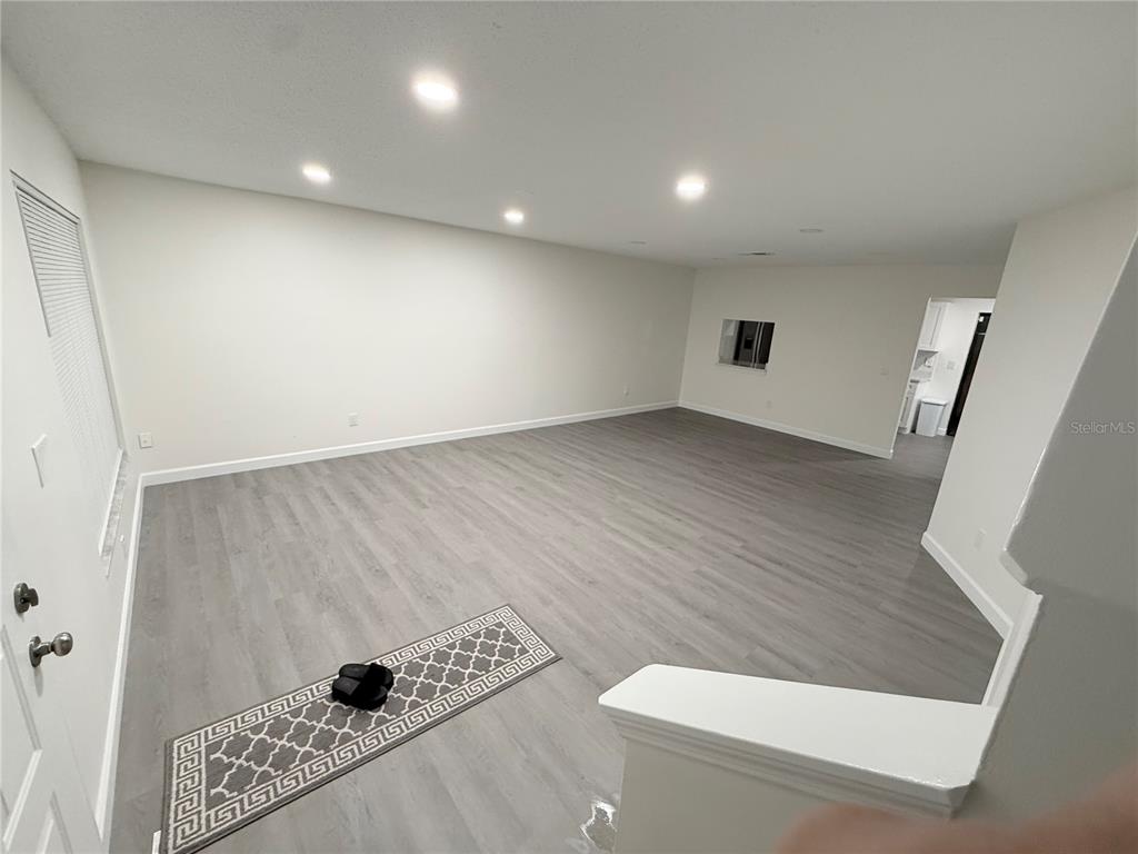 An empty living room features light gray wood-look flooring, recessed lighting, and white walls — 6266 YORKTOWN DRIVE UNIT 179, ORLANDO, FL