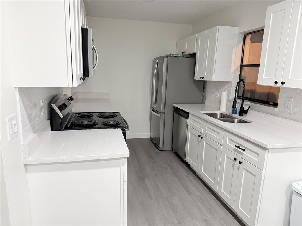 A kitchen features white cabinets, quartz countertops, stainless steel appliances, and light wood-look flooring — 6266 YORKTOWN DRIVE UNIT 179, ORLANDO, FL