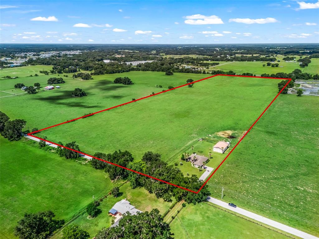 An aerial view shows a large, rectangular grassy pasture outlined in red with two houses — 12604 COUNTY ROAD 103, OXFORD, FL