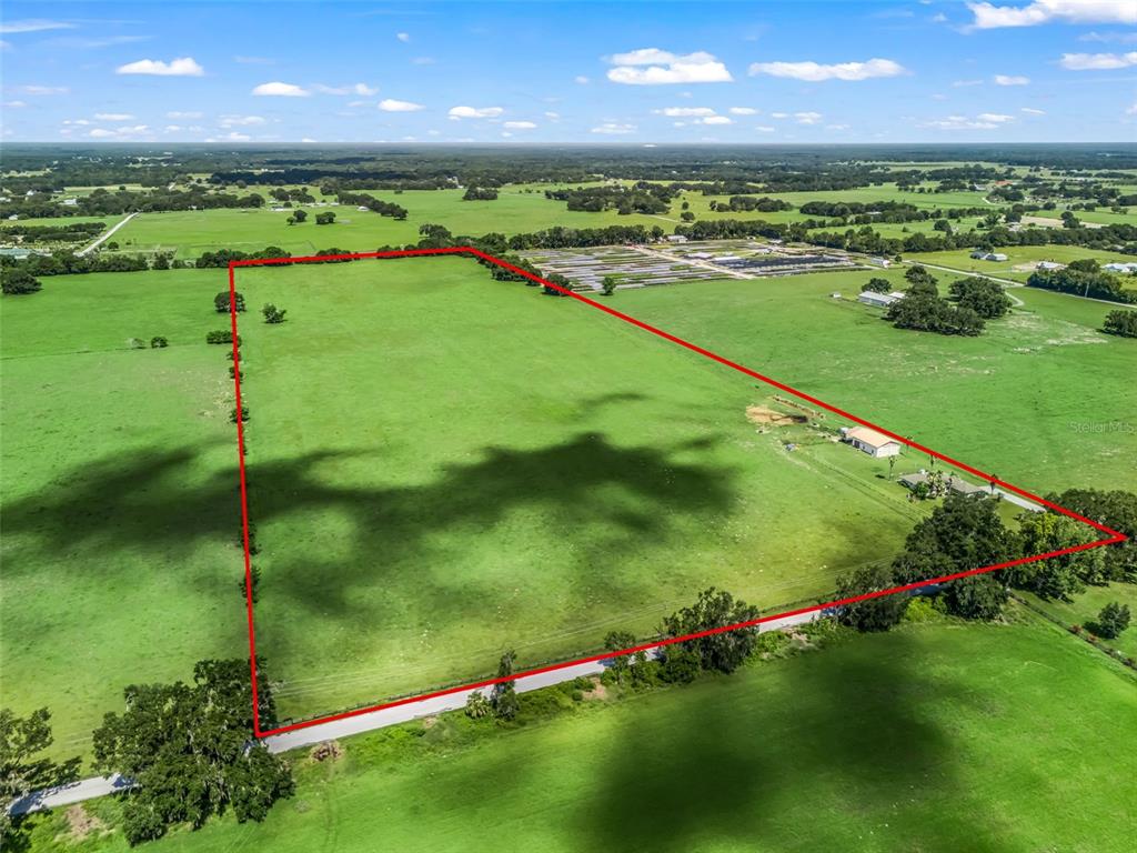 An aerial view shows a large, rectangular grassy pasture outlined in red — 12604 COUNTY ROAD 103, OXFORD, FL