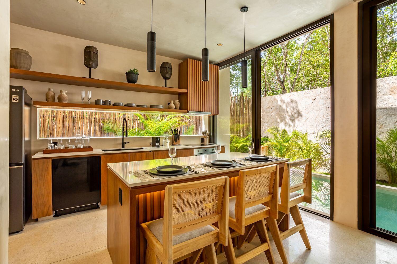 A modern kitchen features a wooden island with cane chairs, open shelving, and floor-to-ceiling windows — Amari Tulum 10 Avenida Norte & Calle Palma, FL