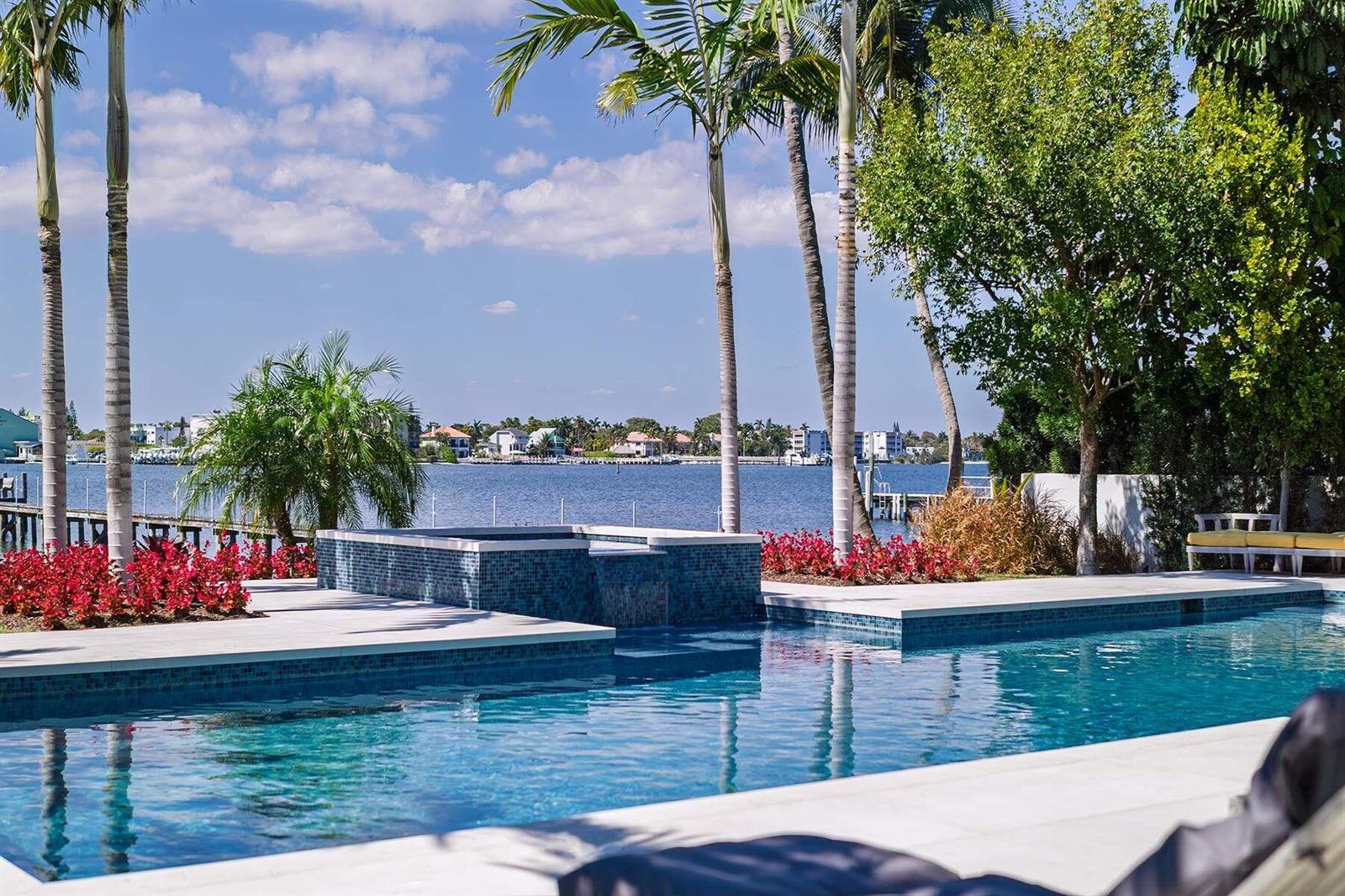 A swimming pool and hot tub overlook a waterfront view with palm trees and landscaping — 807 N Atlantic Drive, Lantana FL 33462, LANTANA, FL