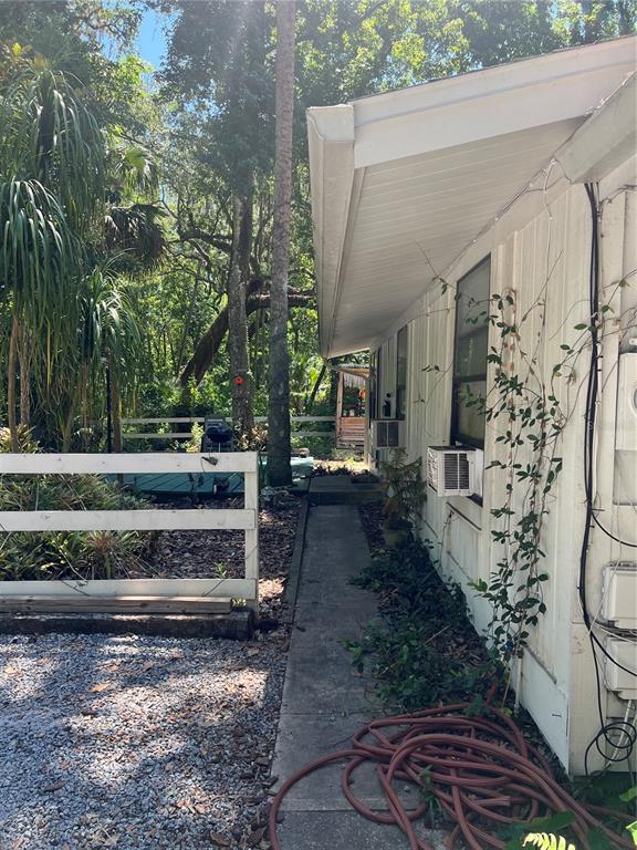 A white house with vertical siding and a gravel driveway sits among mature trees — 1735 TIMOCUAN WAY, LONGWOOD, FL