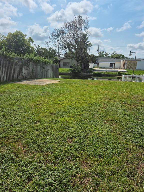 A grassy backyard features a concrete pad, a wooden fence, and a view of a canal — 2604 REEF COURT, ORLANDO, FL