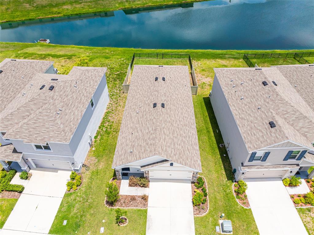 An aerial view shows three suburban houses with shingled roofs and driveways near a pond — 3520 MAPLE GROVE WAY, PLANT CITY, FL