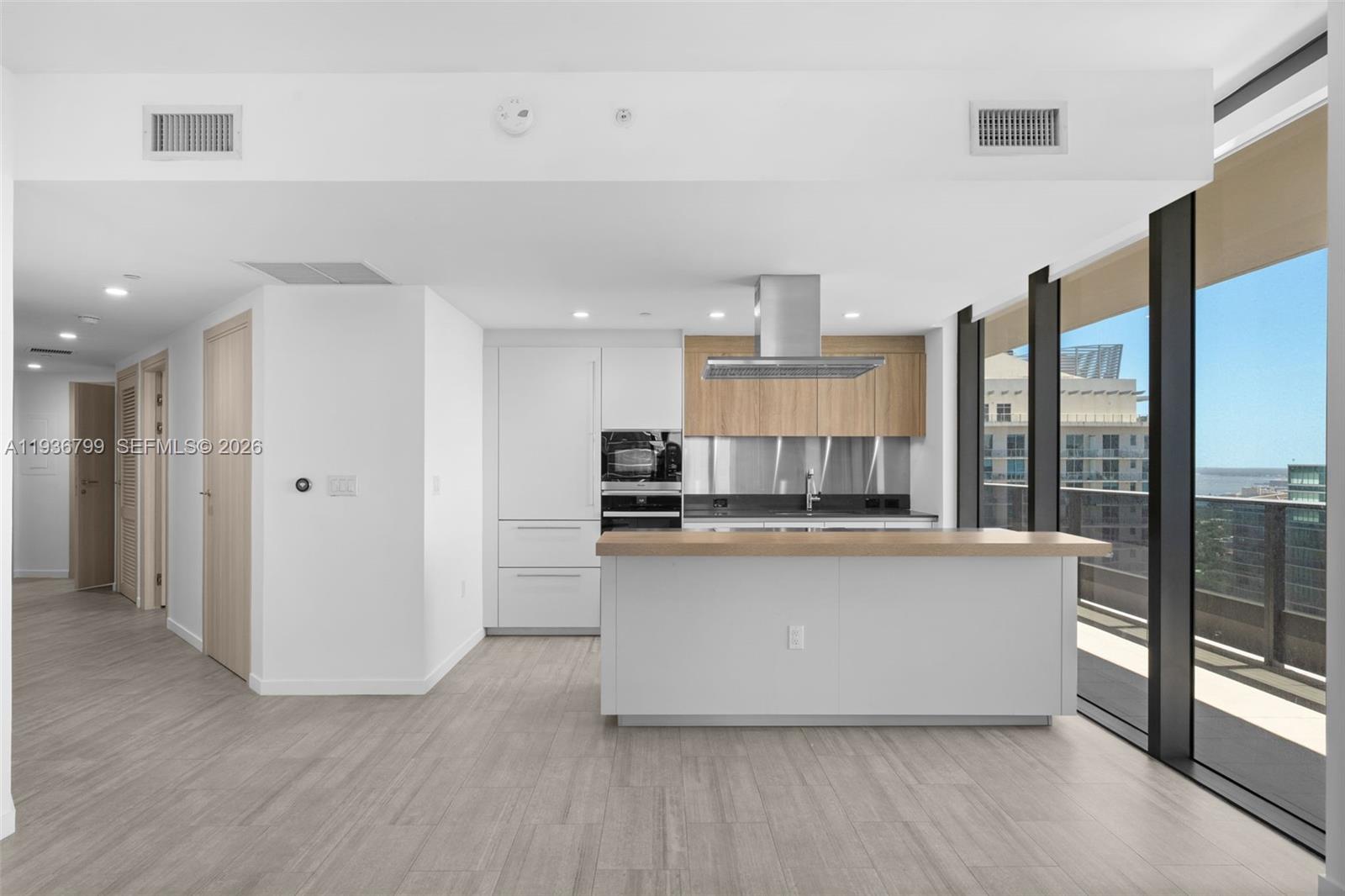 A modern kitchen features white cabinetry, light wood accents, a central island, and floor-to-ceiling windows — 1000 Brickell Plz # 4212, Miami FL 33131, MIAMI, FL