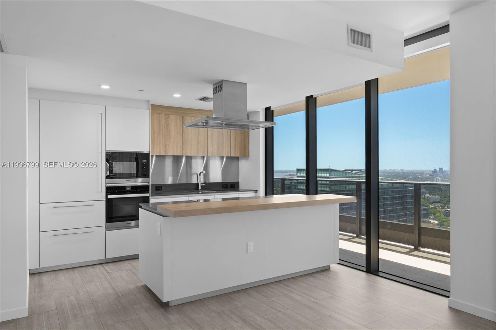 A modern kitchen features white cabinetry, a wood-topped island, and floor-to-ceiling windows with city views — 1000 Brickell Plz # 4212, Miami FL 33131, MIAMI, FL