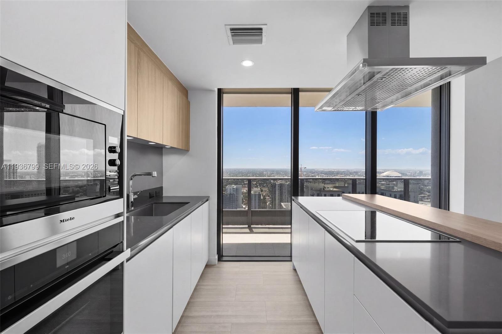 A modern galley kitchen features white cabinetry, wood accents, stainless steel appliances, and city views — 1000 Brickell Plz # 4212, Miami FL 33131, MIAMI, FL