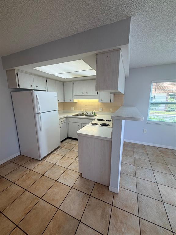 A kitchen with white cabinets, a white refrigerator, tiled flooring, and a breakfast bar — 6050 CHESHAM DRIVE UNIT 5, NEW PORT RICHEY, FL