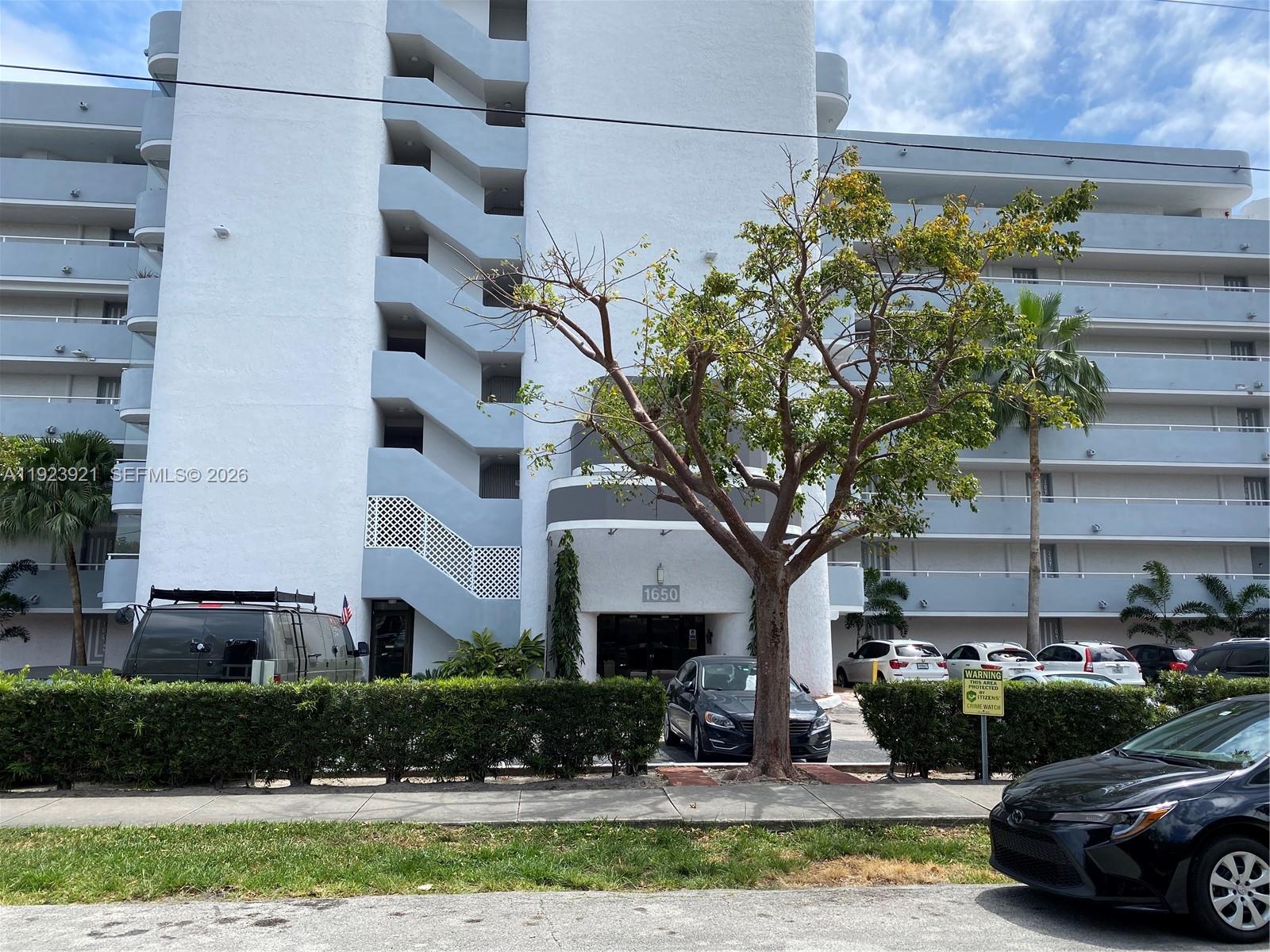 A multi-story white apartment building features an exterior staircase and a tree in front — 1650 NE 115th St # 405, Miami FL 33181, MIAMI, FL