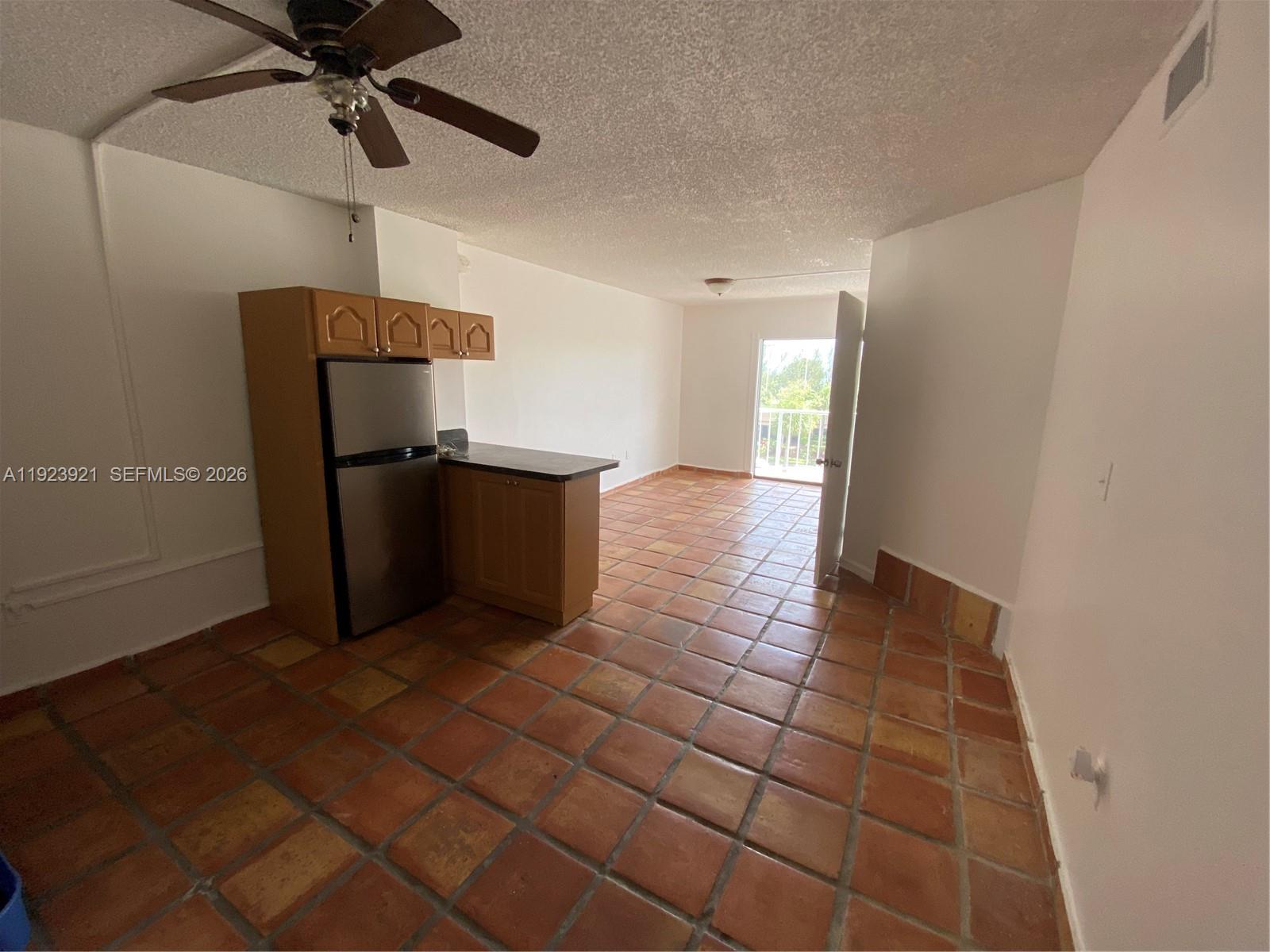 A kitchen with wood cabinets and a stainless refrigerator opens into a tiled living area — 1650 NE 115th St # 405, Miami FL 33181, MIAMI, FL