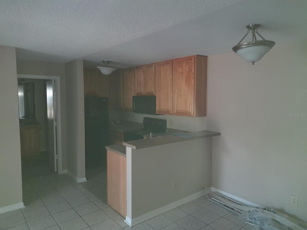 A kitchen with wood cabinets and a breakfast bar overlooks a tiled dining area — 5962 WESTGATE DRIVE UNIT 204, ORLANDO, FL
