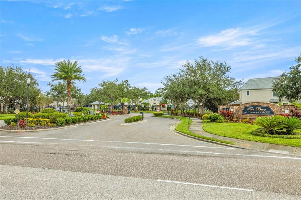 The entrance to The Bay at Cypress Creek features a gated road and landscaping — 26543 CASTLEVIEW WAY, WESLEY CHAPEL, FL