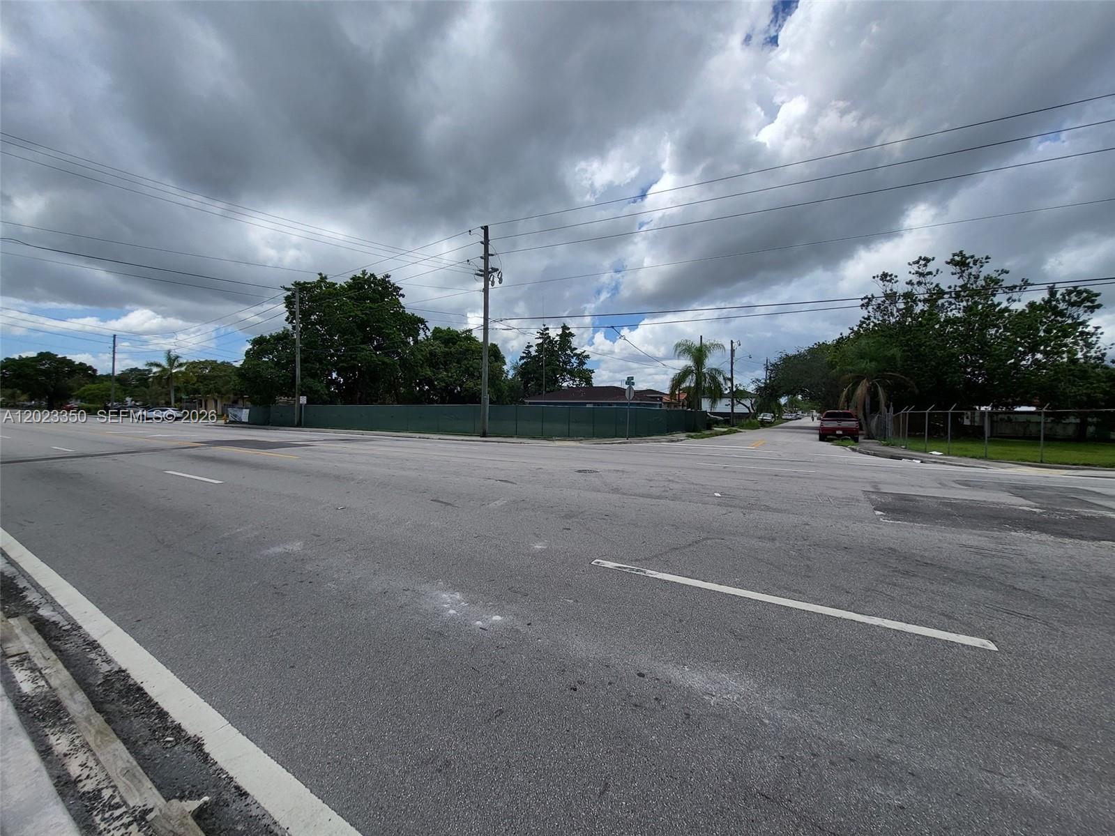An asphalt intersection features a green privacy fence surrounding a vacant lot with trees — 184 ST SW 102 PL, Miami FL 33157, MIAMI, FL