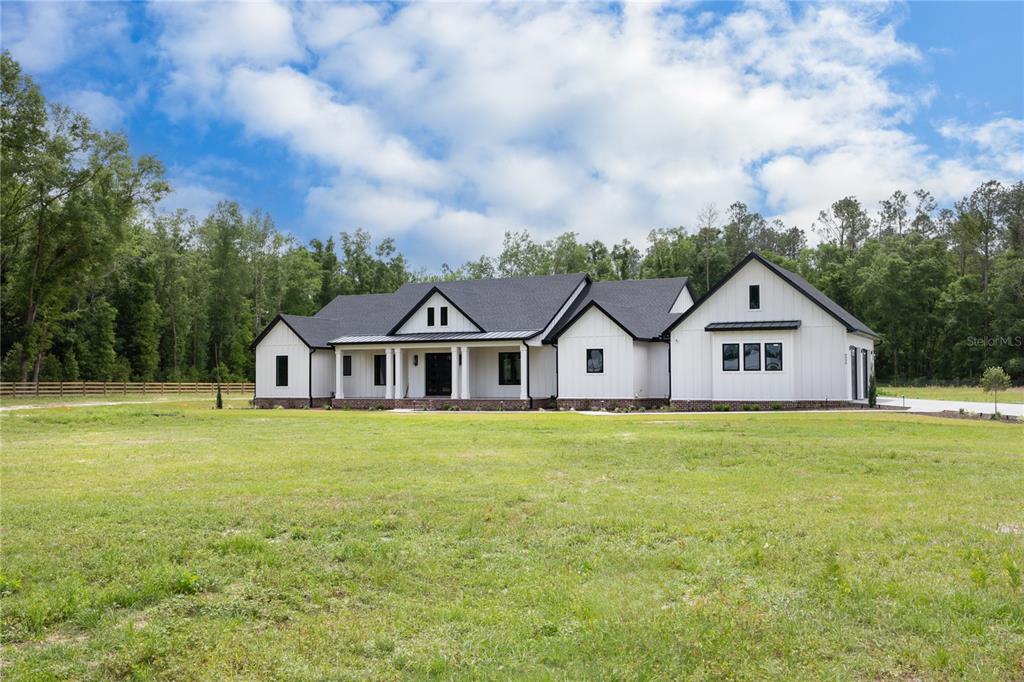 A modern white farmhouse with a dark roof sits on a large grassy lot — 1224 NW 143RD STREET, NEWBERRY, FL