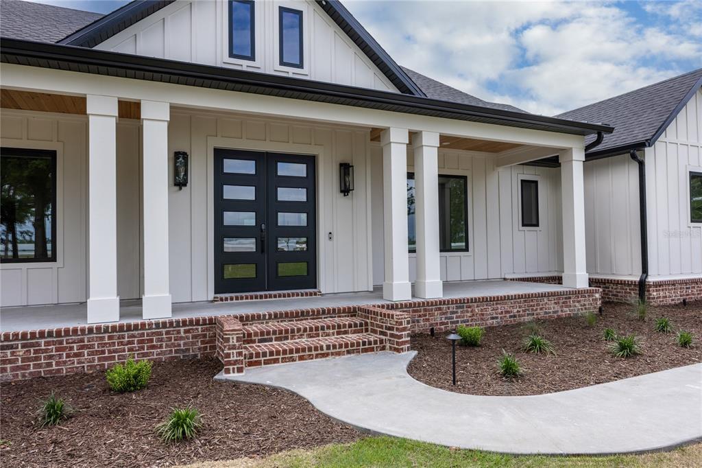 A modern farmhouse exterior features white board-and-batten siding, a brick porch foundation, and double doors — 1224 NW 143RD STREET, NEWBERRY, FL