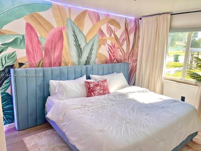 A bedroom features a blue tufted headboard against a tropical leaf mural and white bedding — 601 NW 10th St, Hallandale Beach FL 33009, HALLANDALE BEACH, FL