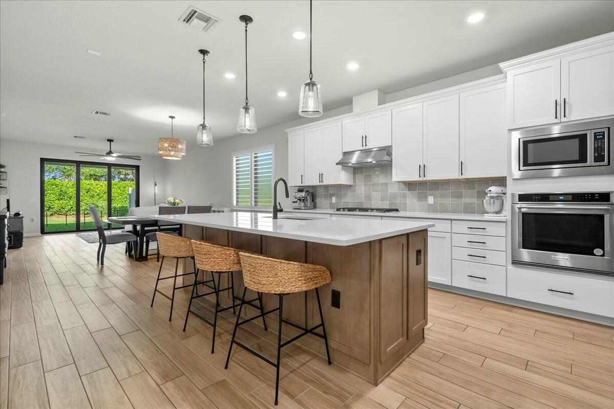 A modern kitchen features a wooden island with wicker stools, white cabinetry, and light-wood flooring — 4801 Chantilly Road, Lake Worth FL 33467, LAKE WORTH, FL