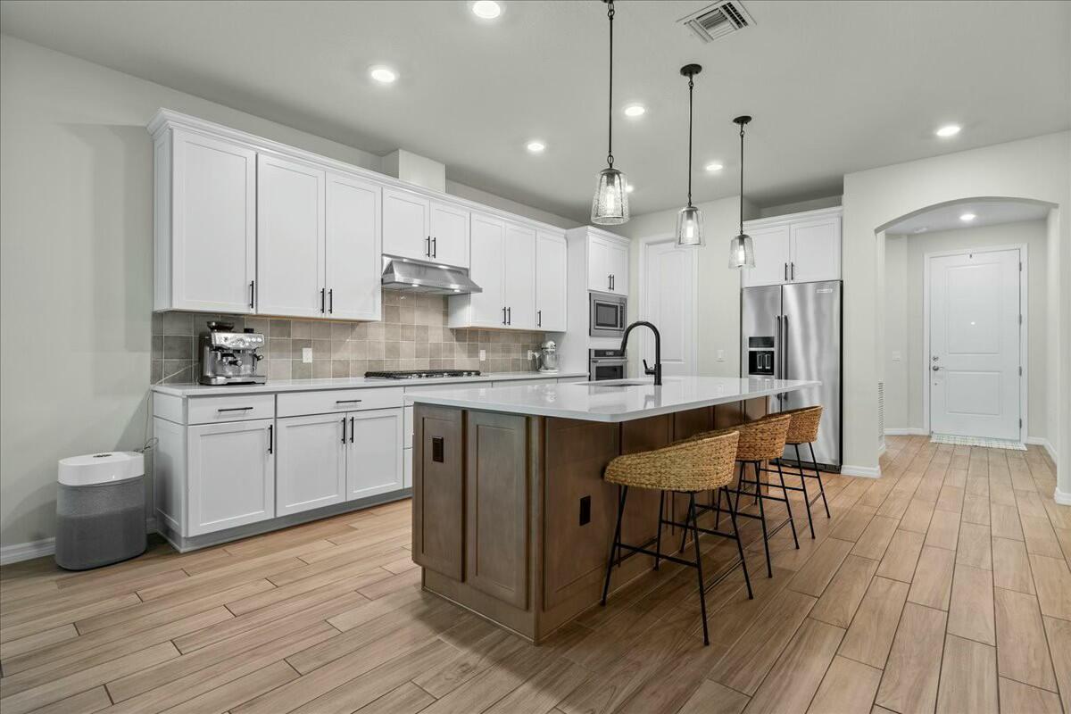 A kitchen features white cabinetry, a wood-toned island with bar seating, and light wood flooring — 4801 Chantilly Road, Lake Worth FL 33467, LAKE WORTH, FL