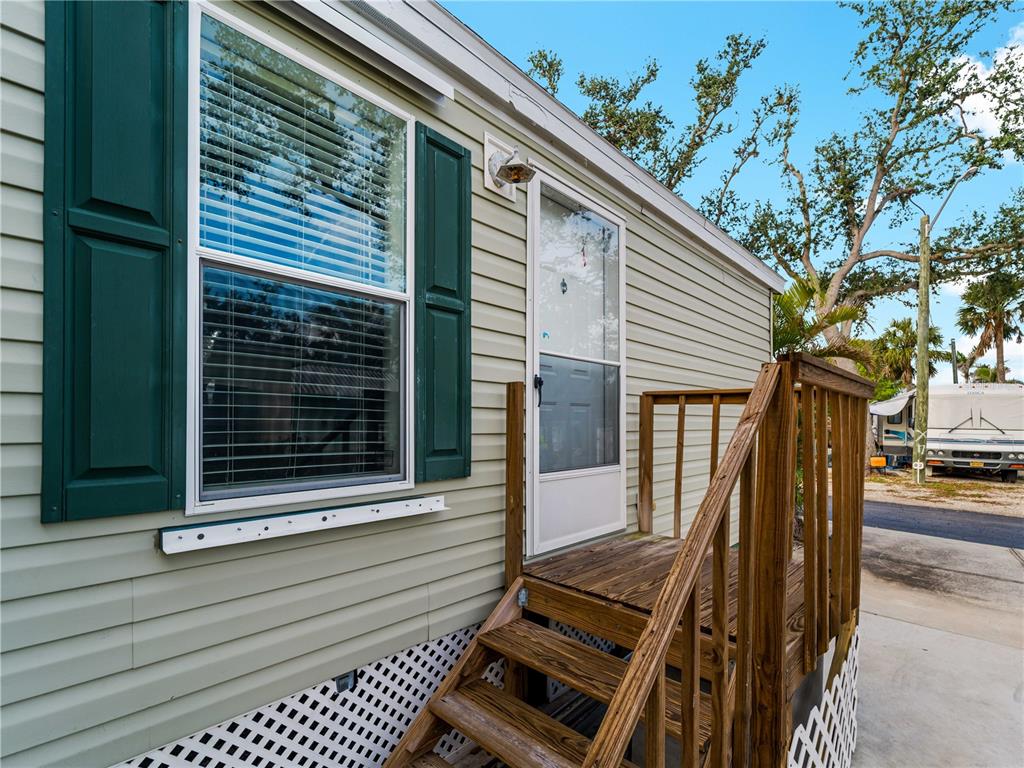 A light green mobile home exterior features a wooden staircase leading to a white door — 1800 ENGLEWOOD ROAD UNIT 24, ENGLEWOOD, FL