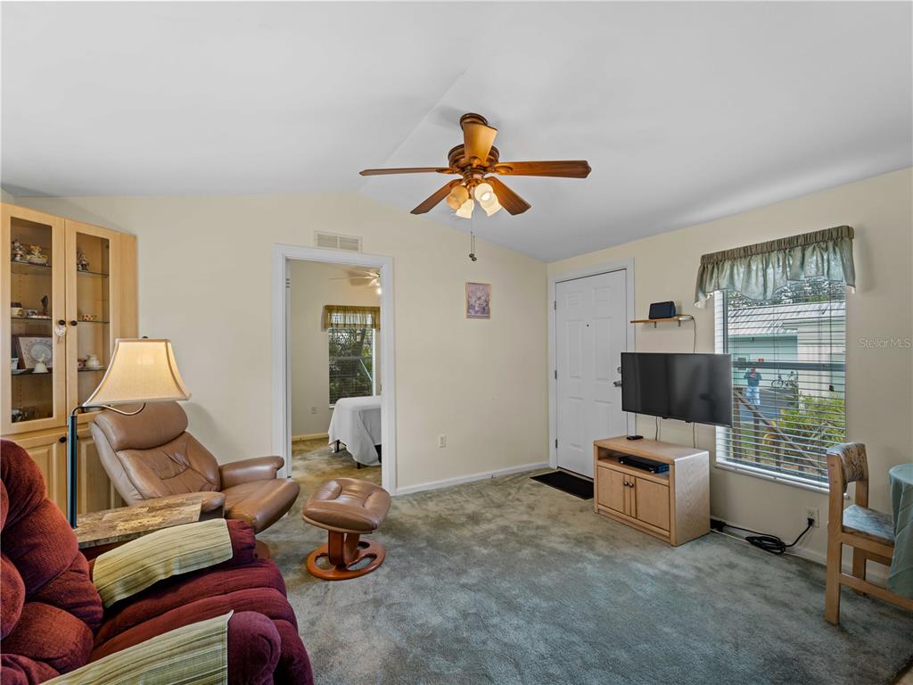 A living room features carpeted floors, a ceiling fan, a television, and a doorway to a bedroom — 1800 ENGLEWOOD ROAD UNIT 24, ENGLEWOOD, FL