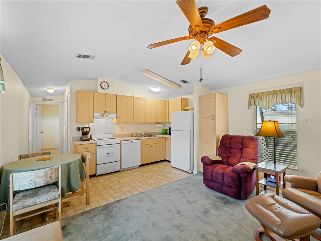 A kitchen with light wood cabinets and white appliances opens into a carpeted living area — 1800 ENGLEWOOD ROAD UNIT 24, ENGLEWOOD, FL
