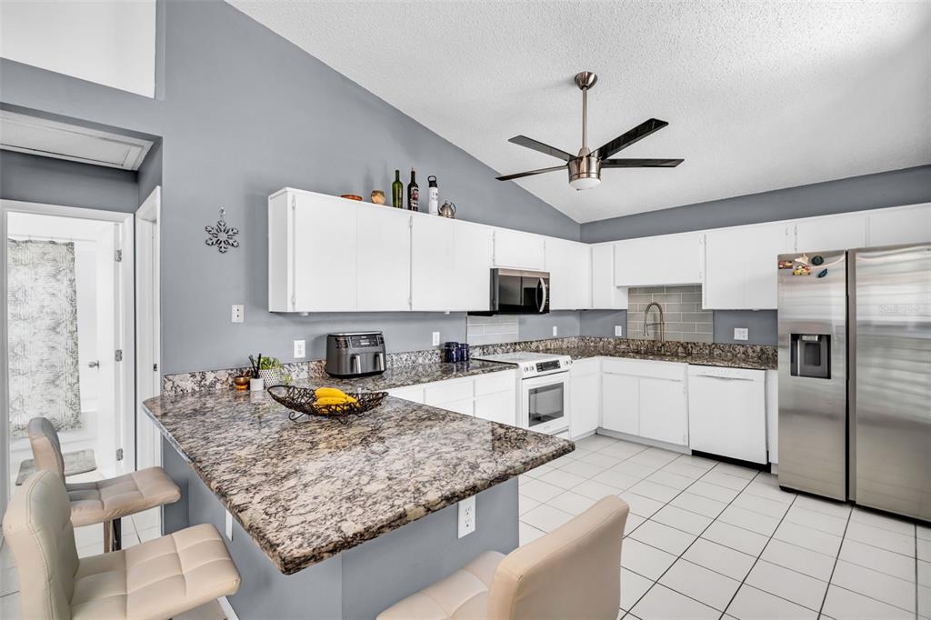 A kitchen features white cabinets, granite countertops, stainless steel appliances, and a breakfast bar — 3067 POINTER DRIVE, PALM HARBOR, FL