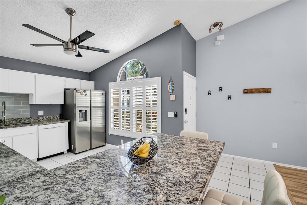 A kitchen features granite countertops, white cabinets, a stainless steel refrigerator, and a ceiling fan — 3067 POINTER DRIVE, PALM HARBOR, FL